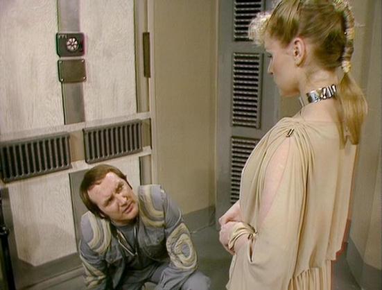 Claude Haiku 4.5 describes the image as: "# Scene Description

This image captures a scene set in what appears to be a spacecraft corridor or futuristic interior. The setting features metallic paneling, ventilation grilles, and institutional-style walls typical of science fiction production design. A wall-mounted clock and various technical fixtures are visible, emphasizing the technological environment.

In the scene, two actors are engaged in an interaction. One actor is positioned on the flo…