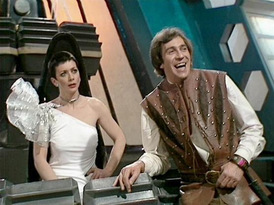 Claude Haiku 4.5 describes the image as: "# Scene Description

This image captures a moment from what appears to be a science fiction television production, set in a futuristic control room or spacecraft interior. The backdrop features the distinctive geometric design typical of 1970s sci-fi sets, with angular panels in teal and neutral tones.

The scene shows two characters in costume. On the left is a character wearing an elaborate white ensemble featuring an impressive sculptural shoulder pi…