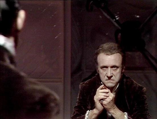 Claude Sonnet 4 describes the image as: "I can see this appears to be from a theatrical or film production, showing someone in period costume in what looks like a dramatic scene. The setting appears dark and atmospheric, with the person positioned in what seems to be an interior space with wooden or metal structural elements visible in the background. The lighting creates a moody, dramatic effect typical of stage or film production. The costume appears to be from an earlier historical period, s…