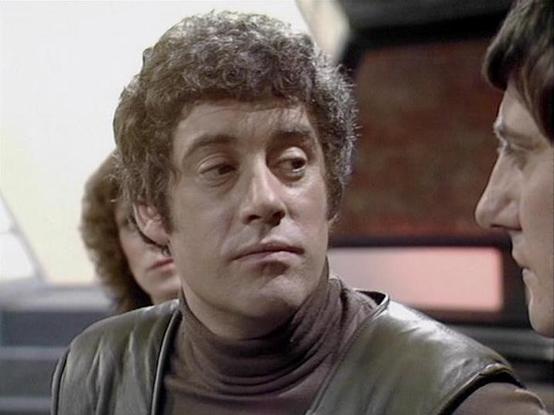 Claude Sonnet 4 describes the image as: "This image appears to be from the classic British science fiction television series "Blake's 7" from the late 1970s. The scene shows what appears to be the interior of a spacecraft, likely the Liberator, with its characteristic futuristic set design featuring curved walls and control panels visible in the background. The lighting and production values are typical of BBC science fiction programming from that era. The setting suggests this is from one of t…