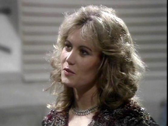 Claude Sonnet 4 describes the image as: "This image shows a scene from what appears to be a British science fiction television production, likely from the late 1970s or early 1980s based on the visual style and production quality. The setting appears to be an industrial or spaceship interior, with metallic surfaces and utilitarian design elements visible in the background.
The scene features distinctive period styling typical of that era's sci-fi productions, with futuristic costume design inc…