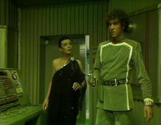 Claude Sonnet 4 describes the image as: "This appears to be a scene from the British science fiction television series "Blake's 7," which aired from 1978-1981. The image shows two characters in what appears to be a futuristic spacecraft interior or space station setting. The scene has the distinctive green-tinted lighting and industrial aesthetic typical of the show's production design.

One character is wearing an elegant black sequined or beaded dress in a classical style, while the other is …