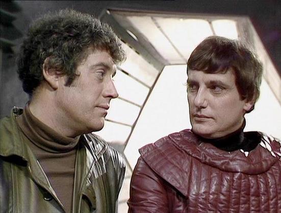 Claude Haiku 4.5 describes the image as: "# Science Fiction Scene

This image captures two men in what appears to be a spacecraft interior, characterized by futuristic geometric ceiling panels that emit bright white light. The setting suggests a science fiction production from the 1970s or 1980s, with its distinctive design aesthetic featuring angular architectural elements typical of that era's space opera aesthetics.

Both individuals are dressed in quilted, form-fitting tunics—one in olive/t…