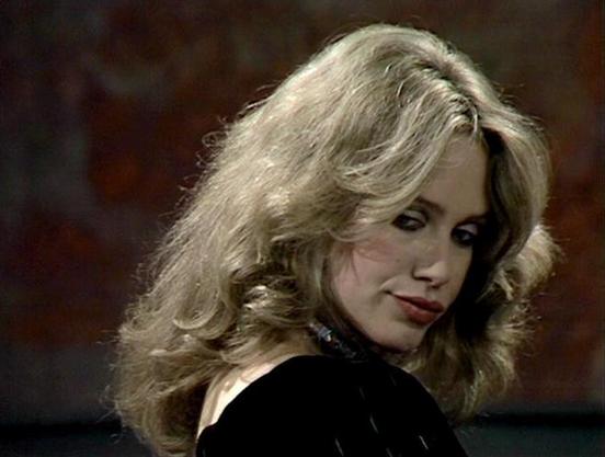 Claude Sonnet 3.7 describes the image as: "The image shows a person with voluminous blonde hair styled in soft waves, looking over their shoulder against a dark, muted background. They're wearing what appears to be a black outfit, possibly from a film or television production from the 1970s or 1980s, based on the styling and film quality. The lighting creates a dramatic mood, highlighting the hair and facial features while keeping the background subdued. The composition has a cinematic quality …