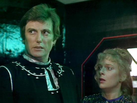 Claude Sonnet 4 describes the image as: "This image appears to be from a science fiction television production, showing two characters in what looks like a spacecraft or futuristic control room setting. The scene has dramatic lighting with green and blue tones that create an atmospheric, otherworldly ambiance. One character wears a distinctive black leather outfit with metallic studs or decorative elements, giving them an authoritative, possibly villainous appearance. The other character has bl…