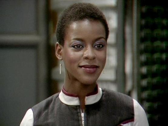Claude Sonnet 4 describes the image as: "This image shows a professional headshot or scene featuring someone in what appears to be a futuristic or science fiction setting. The person is wearing a distinctive uniform with a high collar that has white and burgundy trim details, suggesting this is from a sci-fi television production. The uniform has a sleek, military or space-service aesthetic typical of science fiction shows. The background appears to be an indoor setting with some greenery visib…