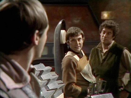 Claude Sonnet 4.5 describes the image as: "This image appears to be from a science fiction television series, showing three actors in what looks like a spaceship or futuristic interior setting. The scene has a warm, brownish color palette typical of 1970s-80s television production.

In the foreground on the left, we see the back of someone's head. In the center, an actor in earth-toned clothing displays a friendly, slightly mischievous smile while holding what appears to be some kind of device …