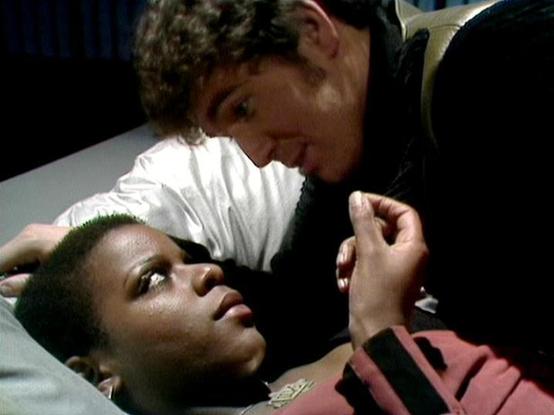 Claude Sonnet 4 describes the image as: "I can see this appears to be from a dramatic production, likely a television show or film, showing an intimate scene between two characters. The setting appears to be indoors with dark lighting creating a moody atmosphere. One person is lying down while another leans over them in what seems to be an emotionally charged moment. The composition and lighting suggest this is from a professionally produced dramatic work, with careful attention to creating ten…