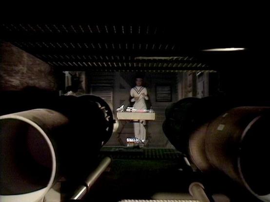 Claude Haiku 4.5 describes the image as: "# Image Description

This appears to be a scene from a classic film, shot from inside what looks like a spacecraft or futuristic vessel. The perspective is from behind two large cylindrical objects or equipment in the foreground, which frame the view toward the center of the compartment.

In the middle distance, a figure dressed in light-colored robes stands at what appears to be a control station or desk. The setting has a distinctly retro-futuristic a…