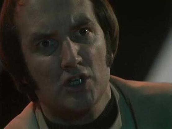 Claude Sonnet 4 describes the image as: "This appears to be a close-up shot from a film or television production, showing a person in what looks like a tense or dramatic moment. The individual has shoulder-length dark hair and is wearing what appears to be a light-colored shirt or jacket with a dark collar. The lighting is moody and atmospheric, with warm amber/orange tones contrasting against darker shadows, creating a cinematic quality typical of thriller or drama productions. The person's ex…