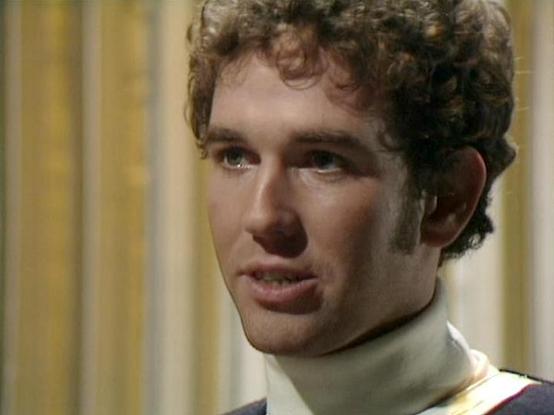 Claude Sonnet 4.5 describes the image as: "This image shows a close-up shot from what appears to be a science fiction television production, likely from the 1970s or 1980s based on the video quality and styling. The actor Steven Pacey is captured in a dramatic moment, wearing a distinctive costume that includes a high turtleneck collar in beige or cream, with white and burgundy trim visible at the shoulders, suggesting a uniform or formal attire typical of space opera productions of that era.

…