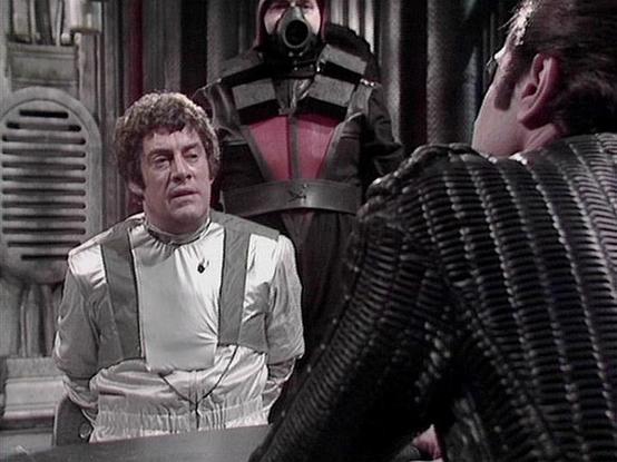 Claude Sonnet 4 describes the image as: "This appears to be a scene from the British science fiction television series "Blake's 7" from the late 1970s. The setting is clearly a futuristic spacecraft interior with characteristic metallic walls and technical details typical of the show's production design.

In the scene, we see characters in what appears to be a tense confrontation aboard a spaceship. One figure is wearing the distinctive white and silver uniform characteristic of the series' Fed…