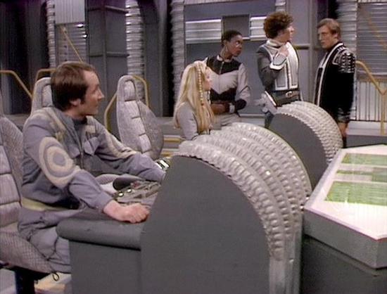 Claude Sonnet 4 describes the image as: "This appears to be a scene from the British science fiction television series "Blake's 7," likely from the later seasons. The setting is the flight deck or bridge of a futuristic spacecraft, featuring the distinctive white and gray aesthetic typical of the show's production design. The environment has a sterile, high-tech appearance with curved architectural elements and what appears to be computer stations or control panels.
The scene shows several cre…