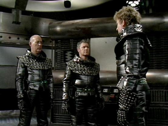 Claude Sonnet 4.5 describes the image as: "This image appears to be from a science fiction production, showing three figures in elaborate black leather costumes with distinctive studded metallic shoulder pieces and armor details. The setting is clearly a futuristic spacecraft or station interior, with metallic walls, industrial-style panels, and what appears to be technical equipment in the background.

The costumes are notable for their militaristic design, featuring multiple studs or rivets c…
