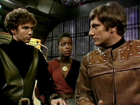 Claude Opus 4.6 describes the image as: "This image is from the British science fiction television series **Blake's 7**, featuring three main cast members on what appears to be the flight deck of the Liberator or Scorpio spacecraft.

**Steven Pacey** (left) plays Del Tarrant, wearing his characteristic dark leather outfit with gold decorative shoulder detailing. He has curly brown hair and is looking toward the right.

**Josette Simon** (center) plays Dayna Mellanby, wearing a dark outfit with …