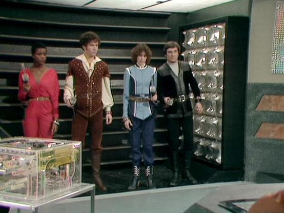 Claude Haiku 4.5 20251001 describes the image as: "# Blake's 7 Scene Description

This image captures a scene from the classic BBC Television series "Blake's 7," showing four characters standing together in what appears to be a spacecraft corridor or command center. The setting features distinctive retro-futuristic design elements typical of 1970s science fiction television, with green-tinted walls, horizontal striping, and metallic decorative panels visible in the background.

The characters a…