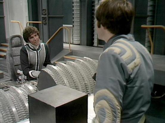 Claude Opus 4.6 describes the image as: "This image is from the classic BBC Television series "Blake's 7." The scene takes place on the flight deck of the Liberator, the main spacecraft used by the show's crew of rebels. The set features the distinctive curved, ribbed console panels and metallic design elements characteristic of the Liberator's interior.

On the left, Steven Pacey is visible as Tarrant, wearing a dark tunic with lighter trim, seated at one of the flight deck stations. He has hi…