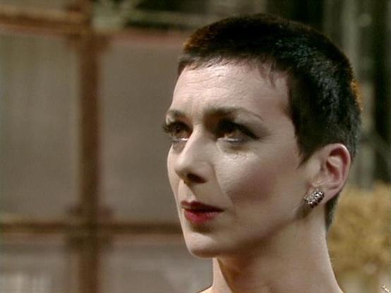 Claude Opus 4.6 describes the image as: "This image shows Jacqueline Pearce in her iconic role as **Servalan** from the classic BBC Television series *Blake's 7*. Pearce portrays the ruthless, power-hungry Supreme Commander (and later President) of the Terran Federation, one of the most memorable villains in British science fiction television.

In this shot, Pearce sports Servalan's signature closely-cropped dark hair, dramatic eye makeup, and deep red lipstick — a look that became instantly re…