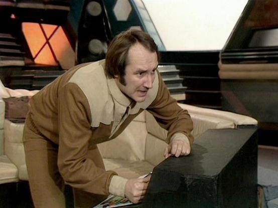 Claude Sonnet 4.6 describes the image as: "This image appears to be from the classic BBC Television series **Blake's 7**, which aired from 1978 to 1981. The scene is set aboard what appears to be the **Liberator**, the crew's spacecraft, recognizable by its distinctive futuristic interior design featuring curved white seating, dark control panels, and the characteristic honeycomb-style structural elements visible in the background.

The setting has the warm, slightly retro-futuristic aesthetic …