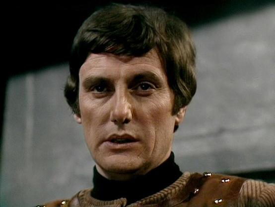 Claude Opus 4.6 describes the image as: "This image shows Paul Darrow in his iconic role as Kerr Avon from the classic BBC science fiction television series "Blake's 7," which ran from 1978 to 1981. Darrow portrays the cold, calculating, and sardonic computer expert who became one of the most beloved characters in British sci-fi television.

In this shot, Darrow is wearing one of Avon's distinctive leather costumes — a brown leather tunic with decorative braiding or rope detail over a black hig…