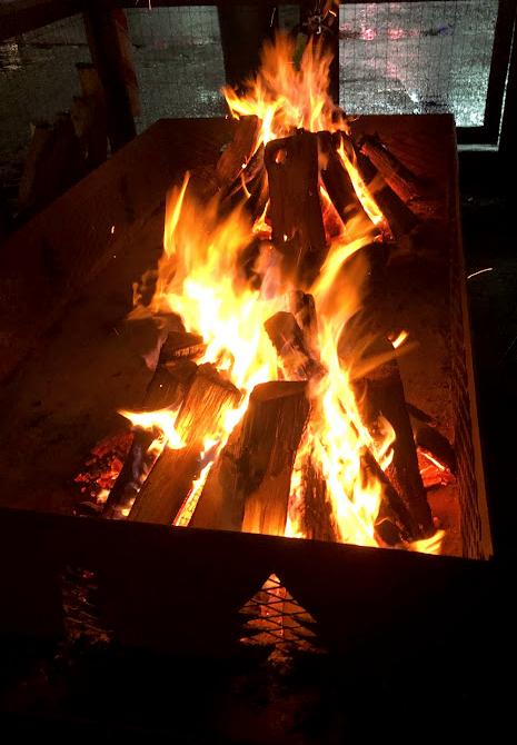 Firepit with a beautiful raging fire with real logs - the rectangular metal fire box has evergreen tree shapes cut out of it... Misty rain cannot overcome this awesome fire...