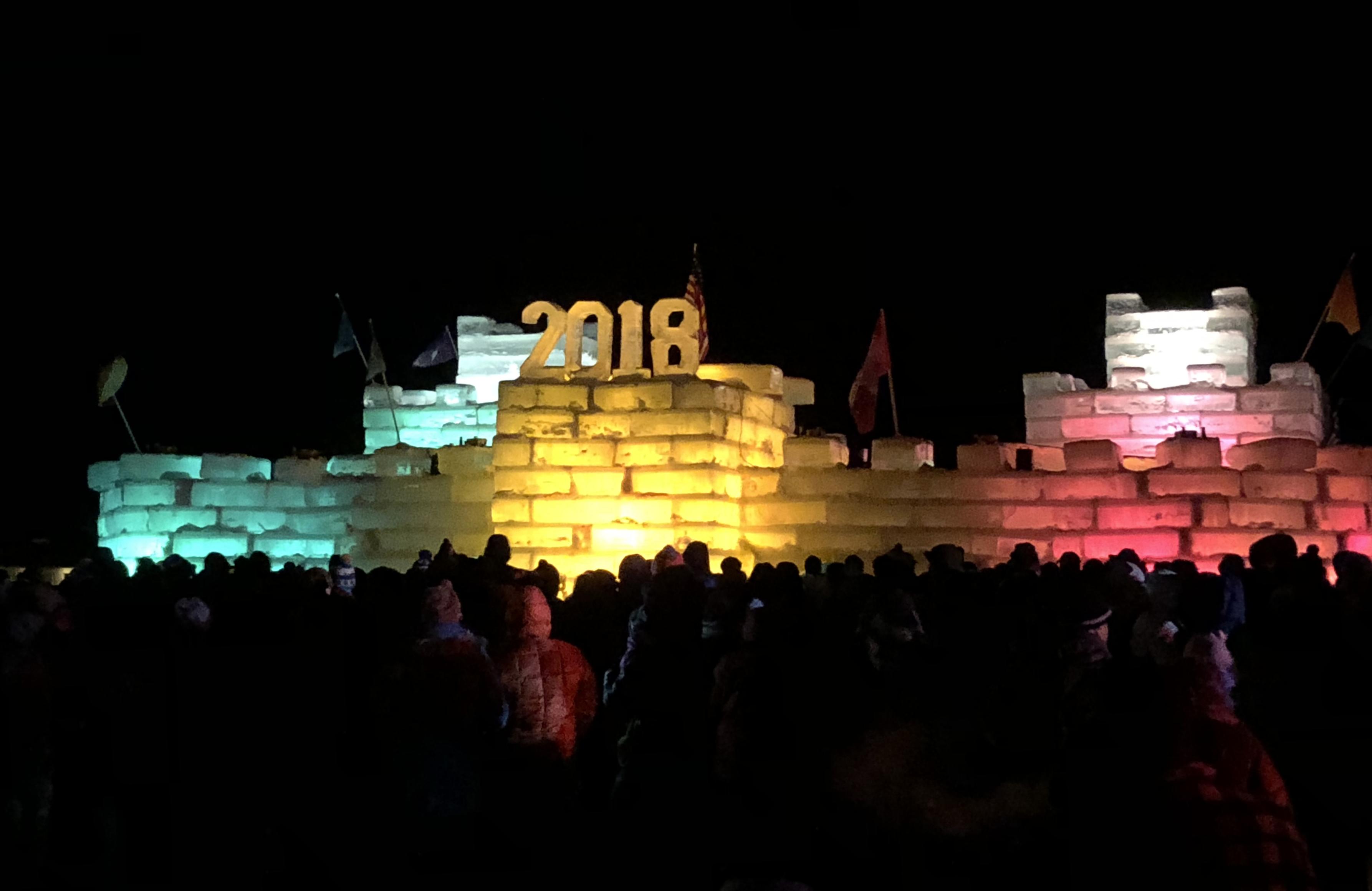Background: Black night sky...
Middleground: Ice palace castle made of large ice blocks taken directly from the frozen Lake Flower, Saranac Lake, NY Adirondack Mountains lit in white, blueish, yellowish, and reddish colors with flags and a "2018" on top...
Foreground: Silhouetted crowd of onlookers waiting in the extreme cold for the upcoming small fireworks show...

Created: 2/03/2018 7:18pm
Aperture: ƒ∕1.8
Exposure: 1∕30 s
ISO: 500
Focal Length: 3.99 mm