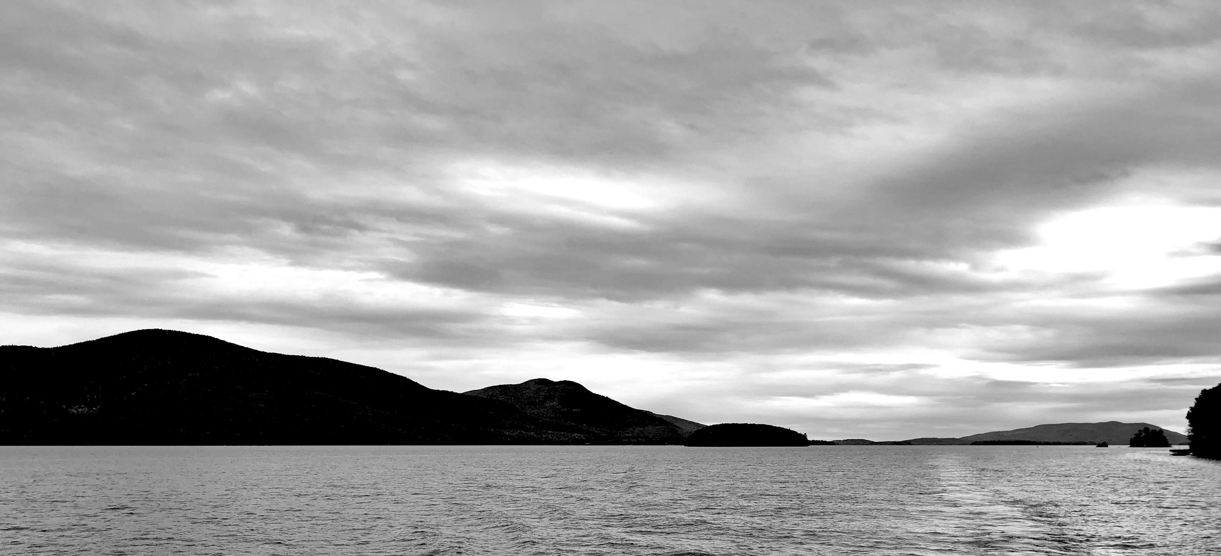 Background: Cloudy sky...
Middleground: On the right, distant small mountains with small lake islands...
Foreground: Lake water... On the left, two peaks of medium sized mountains... A small lake island is center... On the right, a smaller distant island, and another closer island just off frame, with a small boat at the shoreline... 

Created: 10/11/2019 3:36 PM
Aperture: ƒ∕1.8
Exposure: 1∕1499 s
ISO: 20
Focal Length: 3.99 mm