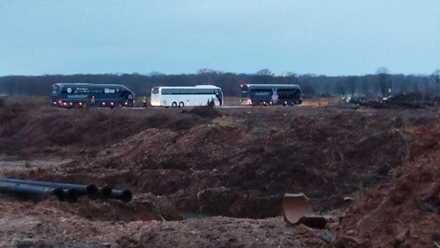 Foto zeigt 3 Reisebusse. Im Vordergrund verwüstete Landschaft, ein Stücke zerbrochenes Abwasserrohr und dünne Pipeline-Rohre.