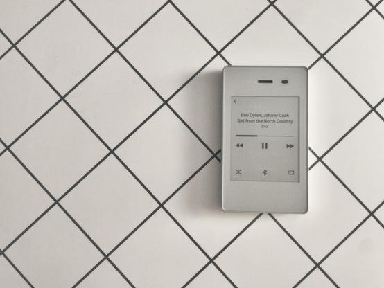 A photo of a phone with an eink display, resting on a table, playing back music.