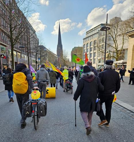 Der Demonstrationszug der Demo "Fukushima mahnt!" von hinten auf der Mönckebergstraße. Es sind einige Anti-Atom Fahnen zu sehen ein Atomfass wird gerollt. Zwei Fahrräder werden geschoben und im Hintergrund ind der Mitte der Kirchturm der St.Petri Kirche.