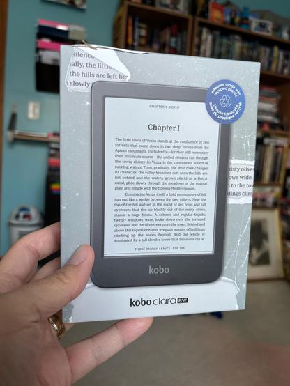 A hand holding a Kobo Clara BW, new in the box (not pictured: Jeff Bezos looking very, very worried at what this represents in terms of potential loss of future profit)