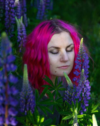 Closeup of a pink haired woman eyes closed surrounded by lupines
