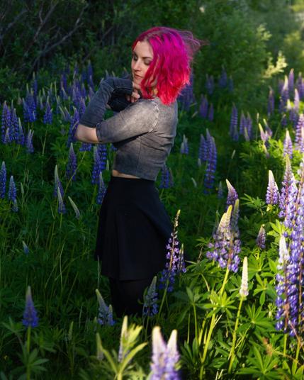 A pink haired woman enjoying sunshine surrounded by lupines