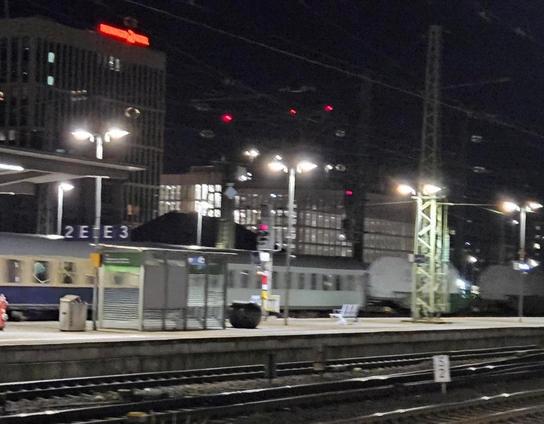 Rechts im Bild zwei Castor Wagons bei der Durchfahrt des Bremer Hauptbahnhof hinter dem Bahnsteig.
Im Vordergrund Schienen, im Hintergrund Gebäude aus Bremen