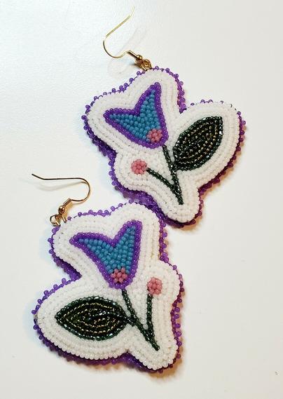 a pair of beaded earrings by kiamichi representing a crocus-shaped flower in blue and purple with a big green leaf on a white background