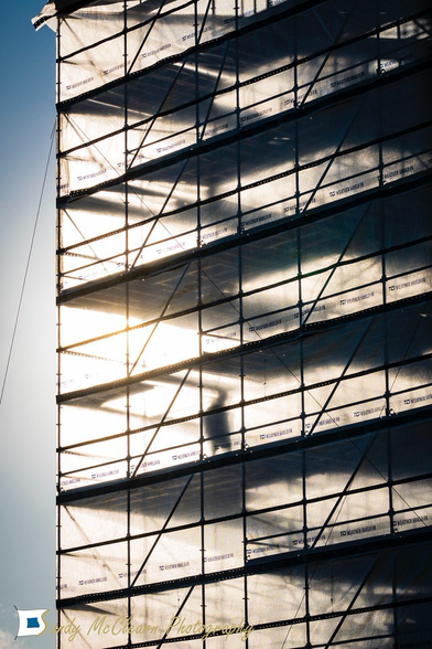 Sun behind a person walking inside plastic-wrapped scaffolding.
