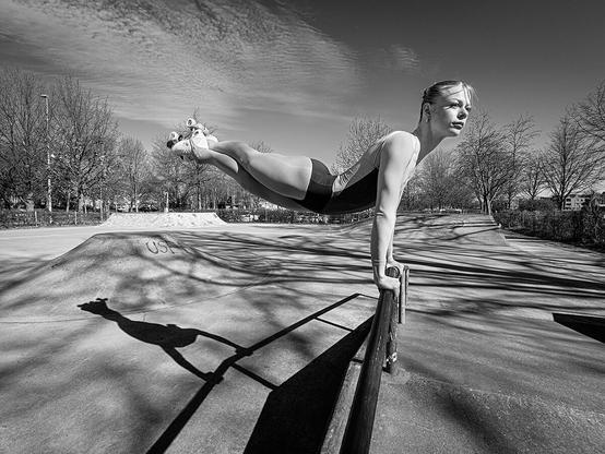 Rollkunstläuferin, die sich mit den Armen auf ein Geländer auf einer Skatebahn stützt und ihre Beine hoch parallel zum Boden hält, die Füße überkreuzt.