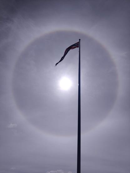 A photograph of the sun showing a clear halo, with a flag in foreground.