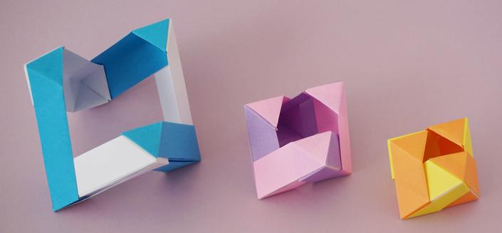 Three origami octahedra on a lilac background. 
The octahedron on the right has a triangular window on the top. The window of the middle octahedron extends onto the adjacent faces by about a quarter. The octahedron on the left has open faces: the edges dominate.
From the left, the colours are blue and white, pink and purple and yellow and orange.
