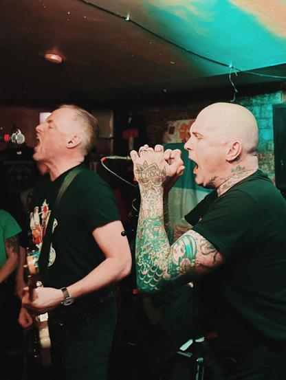 2 men singing on stage. The one on the left (me) is playing a white bass. The one on the right is heavily tattooed.
