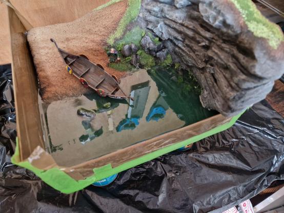 A square diorama featuring a small drakkar (Norse boat) that has been dragged up the shoreline of a small cove and onto the sand. The diorama features a cliff to one side. The model is partially flocked.