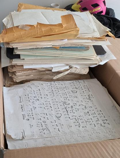 Photo of stacks of paper and booklets (old music scores) in a cardboard box