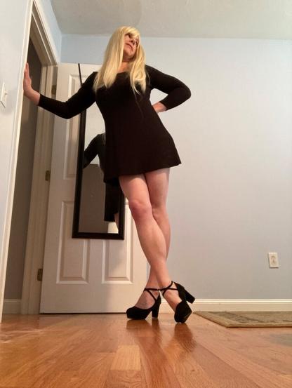 blonde woman with thigh length black dress and black strap high heels.
