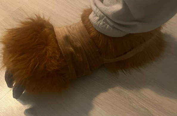 A photo of the upside of fursuit footpaws/shoepaws. The visible fur is darkbrown,  and there gray claws made of minky fabric, on a wooden floor.