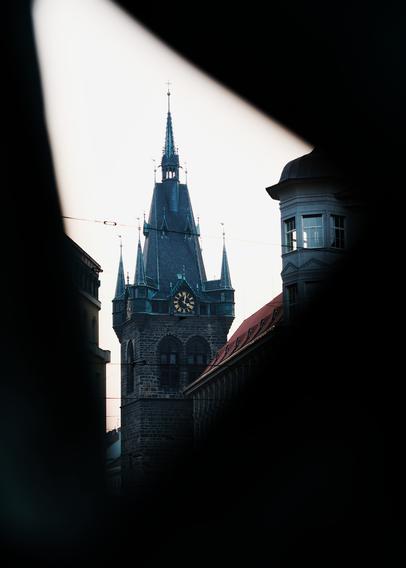 Ein gotischer Turm mit goldener Uhr. Der Blick ist durch den Vordergrund eingerahmt.