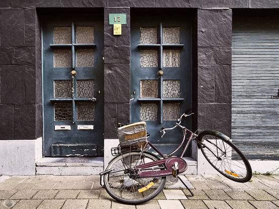 An old dutch bike fallen flat in front of a black facade with two doors in desperate need of some paint.