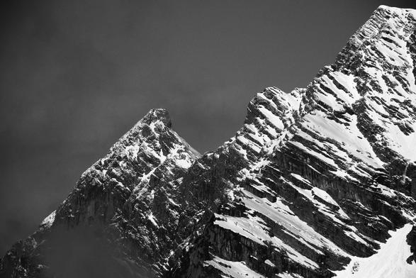 Ein schroffer Berg mit einer Spitze links. Rechts geht es dann noch weiter nach oben. Auf allen flacheren Stellen liegt Schnee. Das Foto ist schwarzweiß.