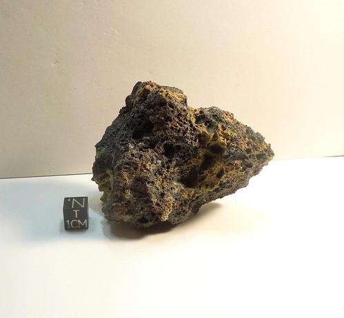 Specimen of Pica comet impact glass shown next to a black centimeter cube.