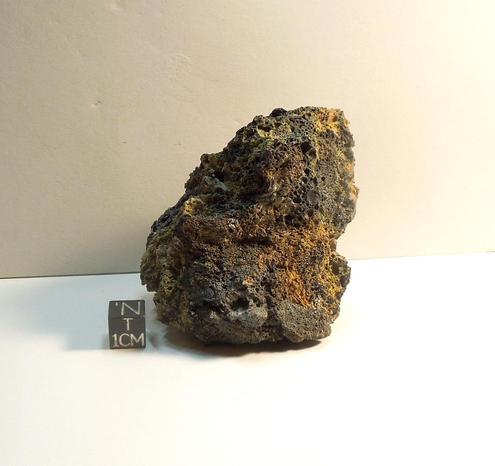 Specimen of Pica comet impact glass shown next to a black centimeter cube.
