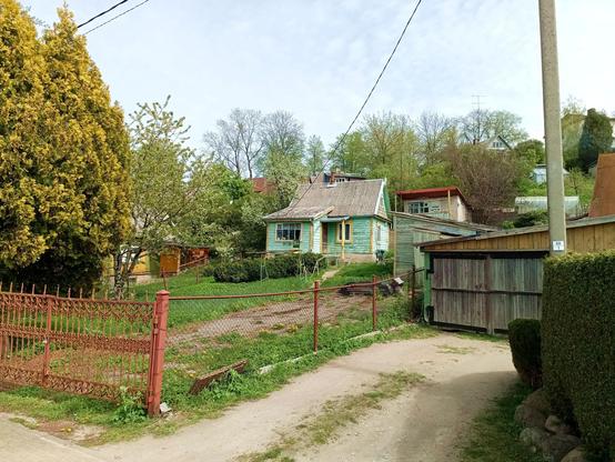An old wooden house on a hill with a brown painted fence and some grass in front. On the right, a wooden garage.